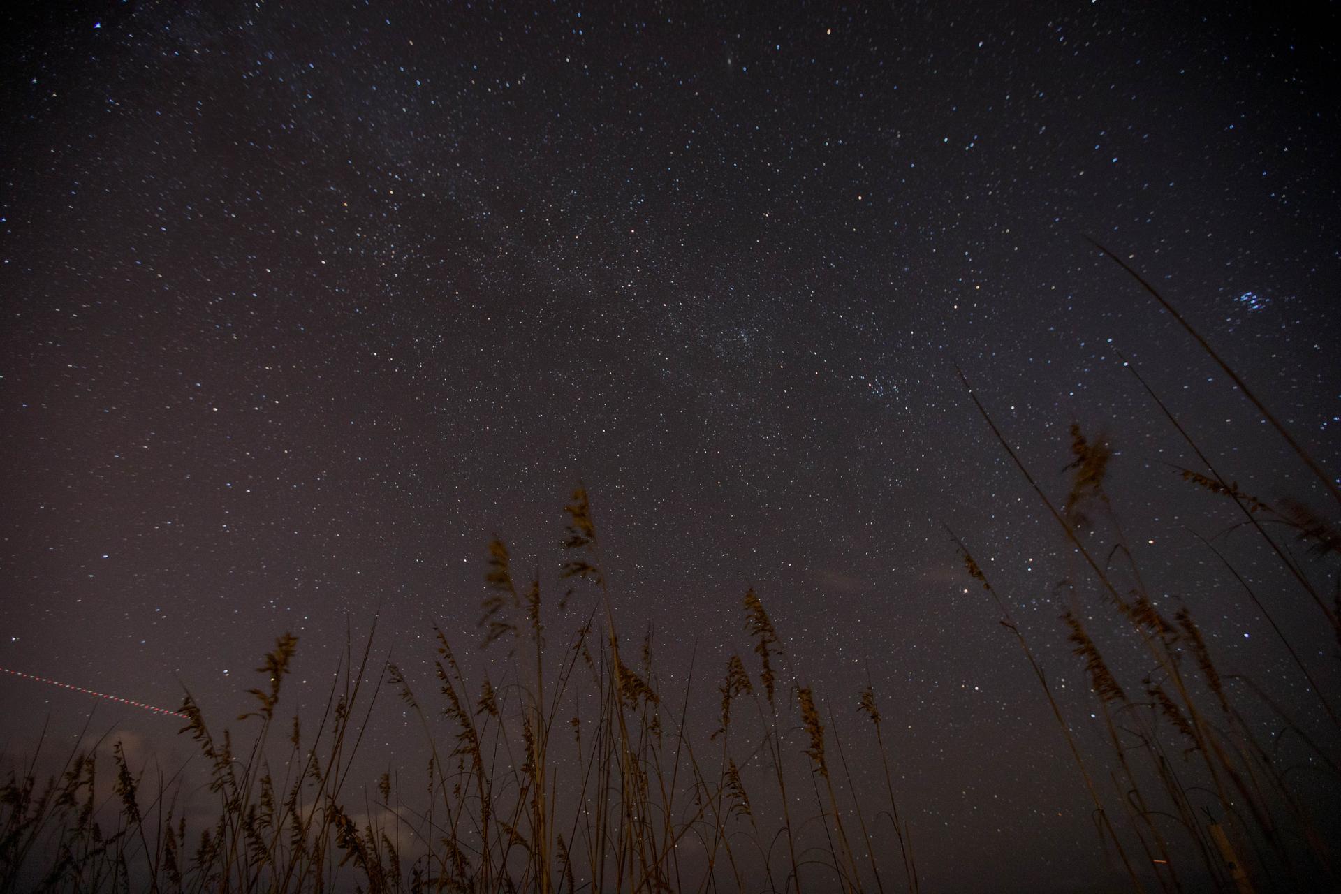 Ciel étoilé traversé par la Voie lactée, avec la traînée lumineuse d'un avion en bas à gauche